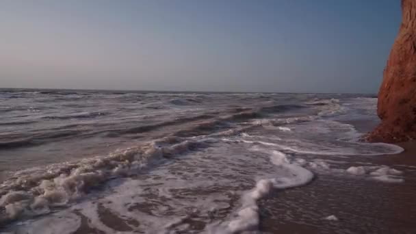 Серфинг коричневого грязного моря, одинокий пляж, волны, когтистая скала, небо — стоковое видео
