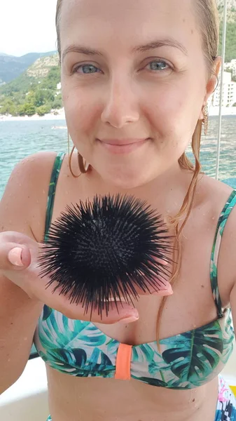 Menina em um maiô segurando um ouriço do mar negro na palma da mão — Fotografia de Stock