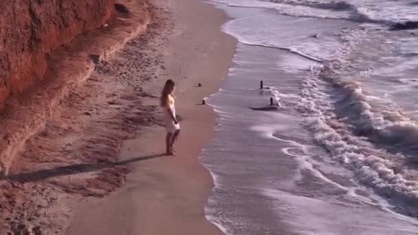 Девушка в белом платье идет вдоль пустынного пляжа к морю, вид сверху — стоковое видео