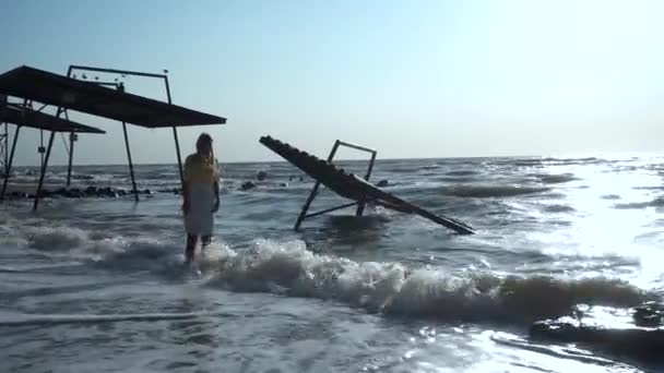 Piękna dziewczyna pochyla głowę, stoi w falach morza, na plaży, w pobliżu pawilonów — Wideo stockowe