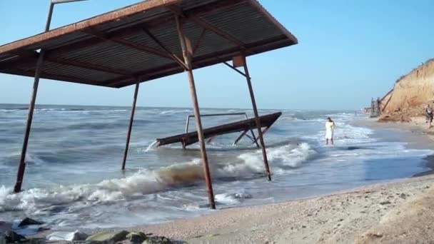 Joven niña está de rodillas en el mar cerca de la vieja, destruido pabellón soviético. plan global — Vídeos de Stock