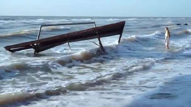 Young girl stands knee-deep in the sea near the old, destroyed Soviet pavilion — Stock Video