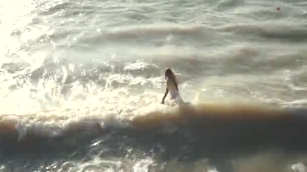Молодая девушка в одежде пытается уйти в грязное, серое море, сквозь волны — стоковое видео