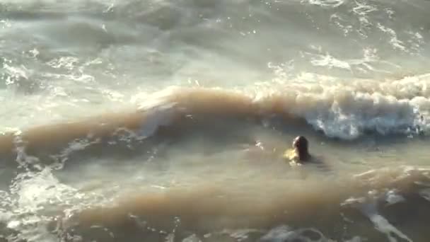 Молодая девушка на плаву в одежде в грязном, сером море, плавающая по волнам — стоковое видео