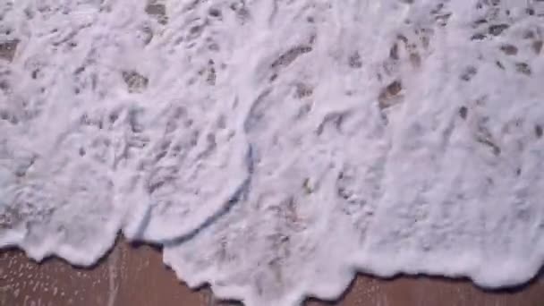 Vitt skum från havets sjudande vågor sprider sig jämnt i bubblor på den våta sanden vid kusten. — Stockvideo