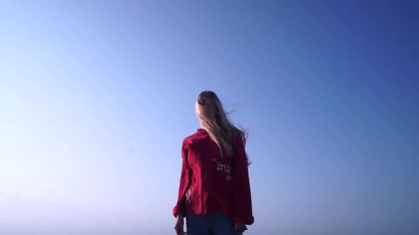 Camera van onder naar boven op een meisje met lang blond haar tegen de lucht — Stockvideo