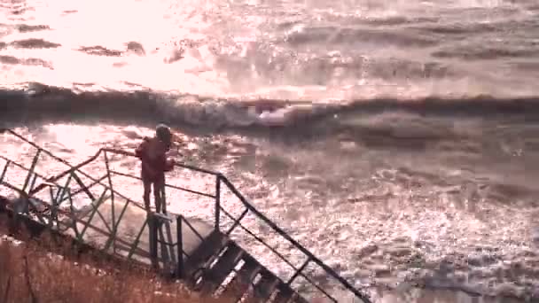 Das Mädchen auf der Plattform blickt von der Treppe auf das tobende schlammige Meer — Stockvideo