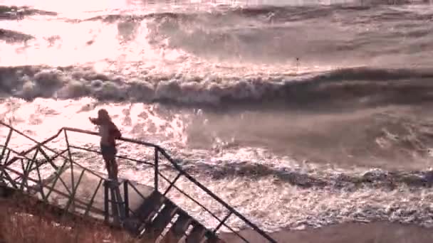 Una chica de pie en las escaleras se congeló en el viento y se envuelve en un suéter — Vídeos de Stock