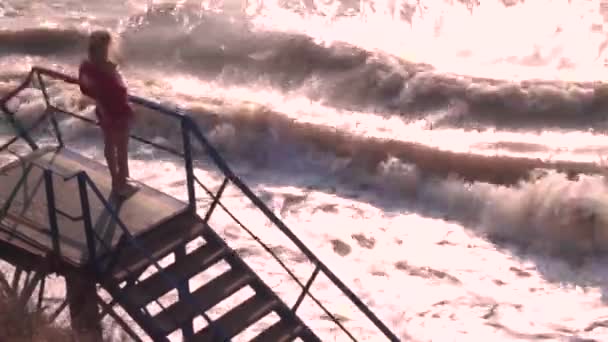 Девушка на ступеньках смотрит на шторм, волны в море — стоковое видео