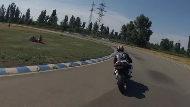 Motorrijder in een blauw professioneel motorpak, een veelkleurige helm, op een zwarte fiets op een racebaan — Stockvideo