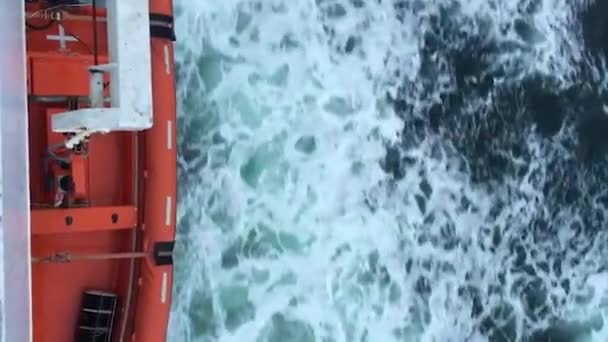 Πορτοκαλί πλοίο που πλέει στον κρύο γαλάζιο ωκεανό, με κύματα και αφρό, εναέρια άποψη — Αρχείο Βίντεο
