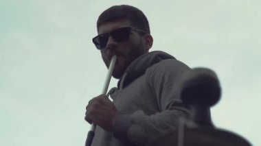 Güneş gözlüklü şık adam beyaz arka planda nargile içiyor.