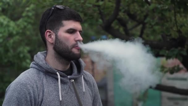 Stylish, young guy in sunglasses smokes a hookah from a pipe, releases smoke — Stock Video