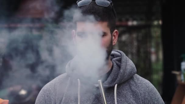 Jeune homme à lunettes fume narguilé, exhale la fumée dans la maison de la caméra — Video