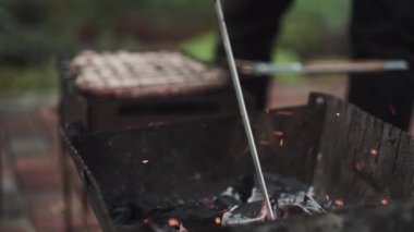 Mangaldaki kömürler ızgarada et pişirmek için şömine demiriyle çevirilir.