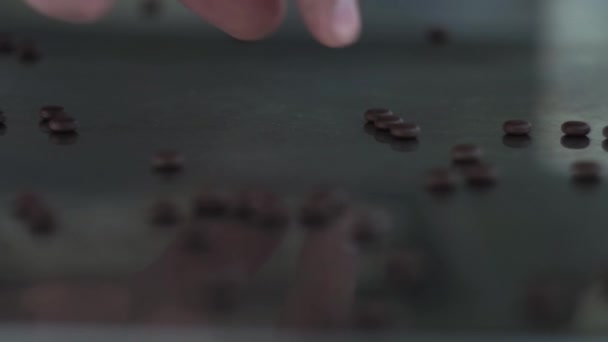 Az ujjak felszedik a kis barna tablettákat szétszórva egy fém, tükör asztalon — Stock videók
