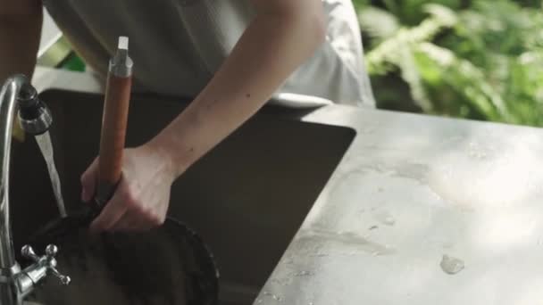 Mujer manos esponja espuma de la cacerola, bajo el agua corriente, mesa de metal, cocina, casa de campo de verano — Vídeo de stock