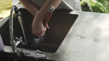 Kadın elleri tavadan köpük temizler, suyun altında, metal yıkama leğeni, mutfak, yazlık ev.