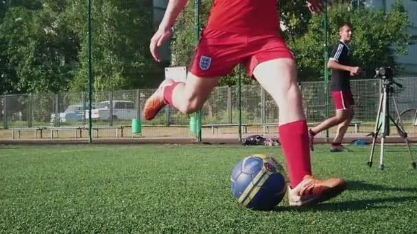 ZAPOROZHYE, UKRAINE - 2020年7月8日:赤いスニーカーの若い男がサッカー場でボールを激しく打ち負かします。緑の草白い靴下強いキックサッカー — ストック動画