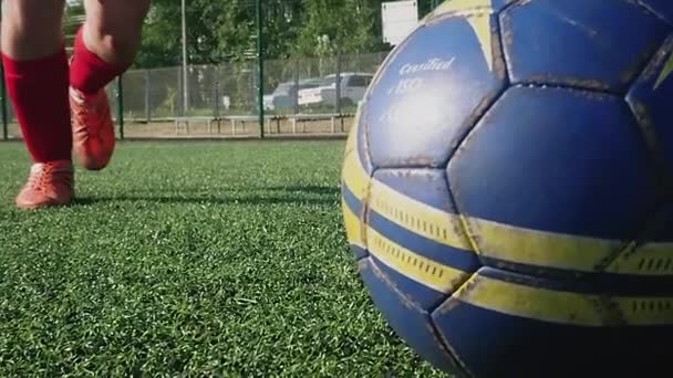 ZAPOROZHYE, UKRAINE - 8 JULI 2020: Jongeman in rode sneakers slaat zwaar op een bal op het voetbalveld. Groen gras, witte sokken, een sterke trap, voetballen — Stockvideo