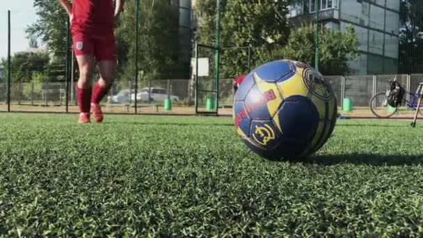 ZAPOROZHYE, UKRAINE - 8 de julho de 2020: Jovem de tênis vermelho bate fortemente uma bola no campo de futebol. Grama verde, meias brancas, um chute forte, jogando futebol — Vídeo de Stock