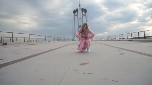 Девушка в розовом платье на корточках позирует для фото, видео клипа на стройке — стоковое видео