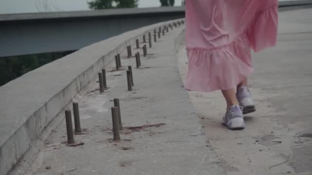 Девушка одна идет по пустынной, бетонной дороге, незавершенному мосту — стоковое видео