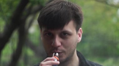 Adam kameraya elektronik bir sigaradan beyaz duman üflemiş.