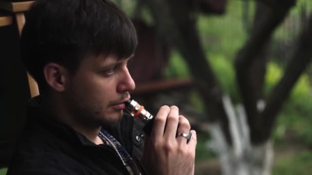 Guy smokes a vape in country, releasing a white cloud of smoke in full screen — Stock Video