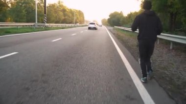 Bir atlet şafak vakti asfaltta pistte koşar. Arabalar geçiyor.