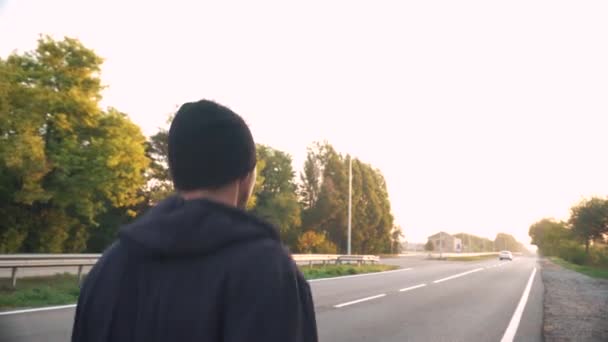 Primer plano, atleta corre a lo largo de la pista, al amanecer, en el asfalto. Los coches están pasando. — Vídeos de Stock