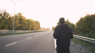 Yakın plan, atlet pistte koşuyor, şafakta, asfaltta. Arabalar geçiyor.