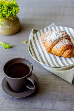 Gri bir arka planda kruvasan ve kahve. Çiçekler. Kahvaltı.