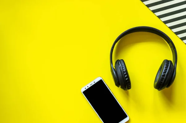 Auriculares negros y un teléfono sobre fondo amarillo. Concepto mínimo. Diseño. Puesta plana . — Foto de Stock