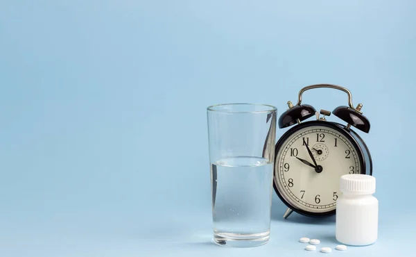 Jar of pills, water and a clock on a blue background. Time to take pills. Insomnia. Copy space