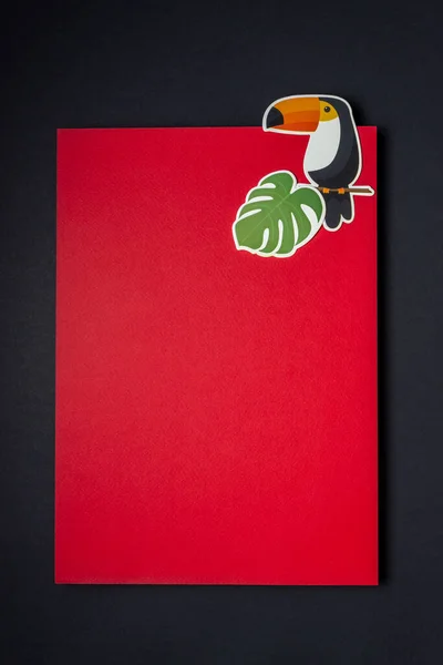 Paper bird and palm tree branch on a red black background. Minimal concept. Copy space