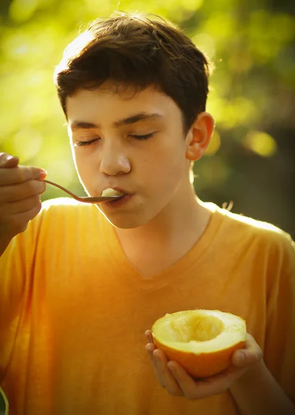 Tonåring pojke äter halv skär mogen melon med sked — Stockfoto