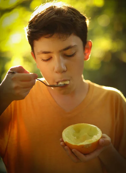 Tonåring pojke äter halv skär mogen melon med sked — Stockfoto