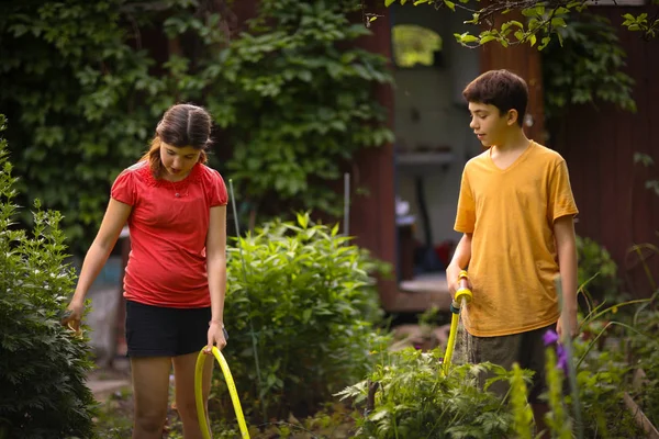 Kid hands hold hose with squirting water on the summer sunny green garden — Stock Photo, Image