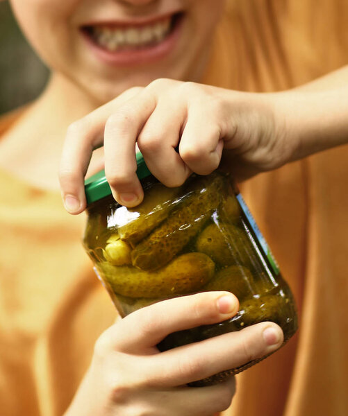 boy with strain grimace try to remove cover from cucumbers jar