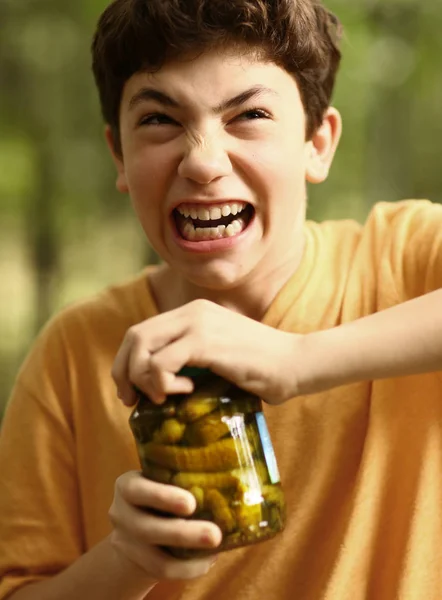 Boy with strain grimace try to remove cover from cucumbers jar — Stock Photo, Image