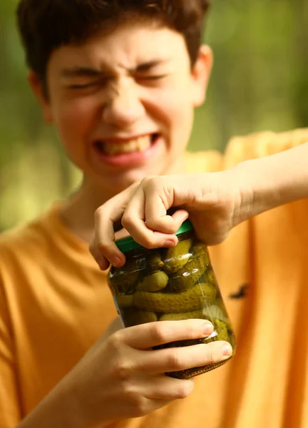 男孩与应变鬼脸试着从黄瓜罐子里取下盖子照片 — 图库照片