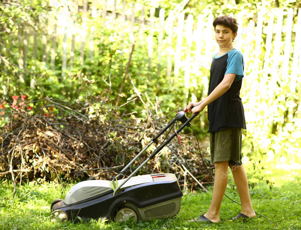 teenager boy mooving lawn in green summer garden