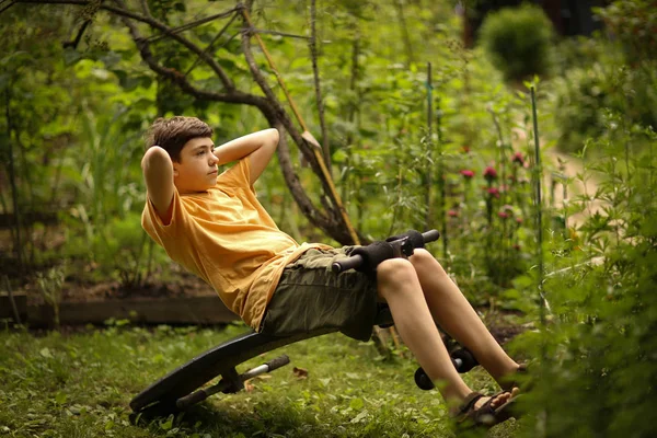 十几岁的男孩做推普拉提腹部演习便携式训练师关闭照片在夏季花园背景 — 图库照片