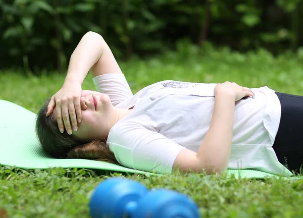 teenager girl lay exhausted on gym rag with dumbbell after train