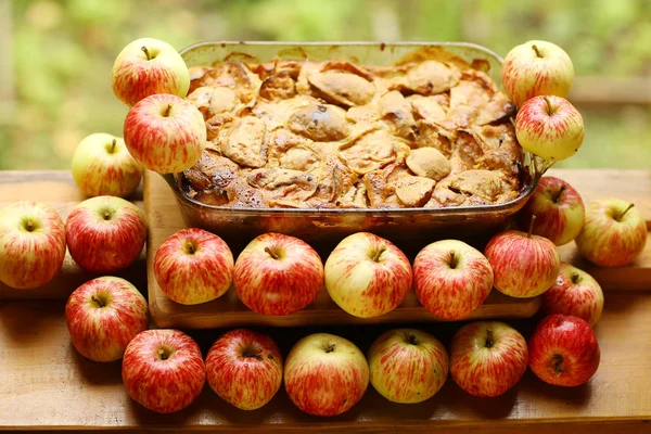 Кусочки свежего яблочного пирога среди сырых яблок в стиле кантри — стоковое фото