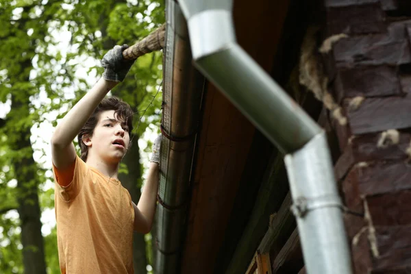 青少年男孩用旧叶清扫屋顶的特写照片 — 图库照片