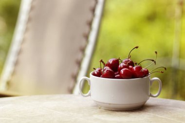 Sağlıklı kahvaltı - kasede tatlı kiraz. Yeşil bahçedeki fotoğrafı kapat ve şezlonga geç.