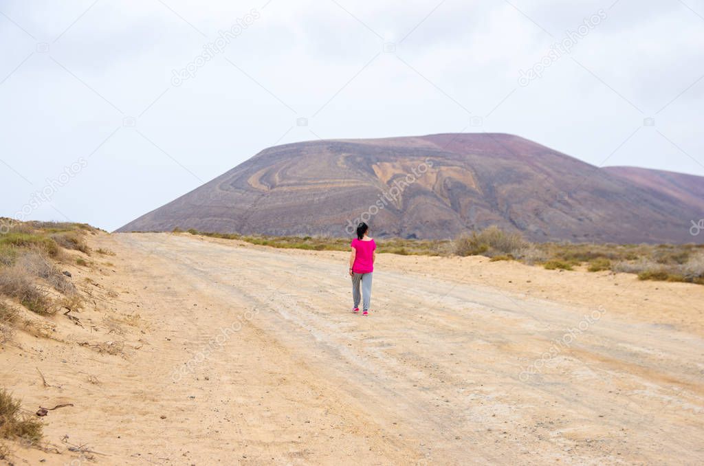 Woman in pink walking on a sandy path towards a volcano