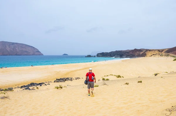 Man in het rood met hoed wandelen op het zand naar de zee — Stockfoto